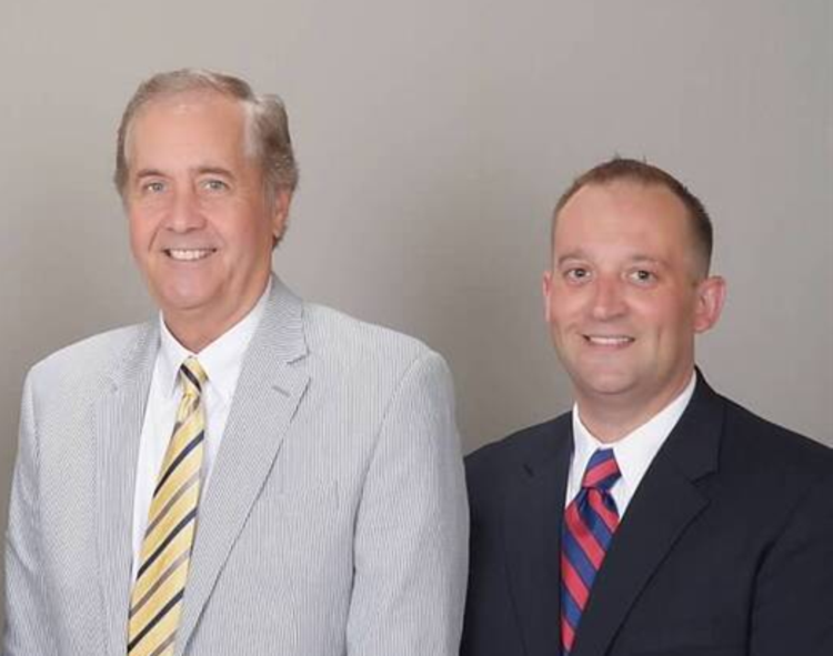 Three white business professionals wearing business suits, standing in front of a gray background.
